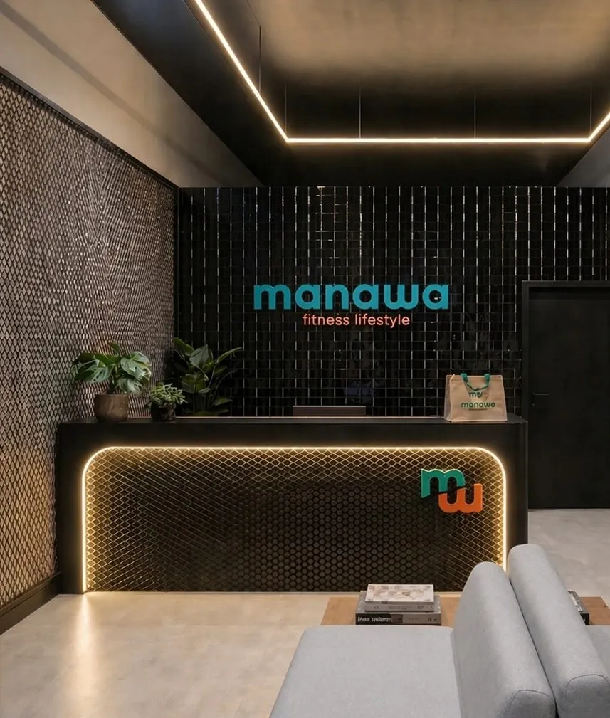 Recepção da Manawa, com parede de tijolo escuro, balcão iluminado e a marca em neon sobre o fundo